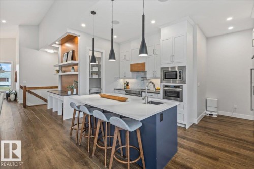 Modern kitchen featuring a large central island with seating, white shaker-style cabinetry, stainless steel appliances, and wood-finish flooring - 10611 146 Street Nw, Edmonton, AB - Indoor Photo Showing Kitchen With Upgraded Kitchen