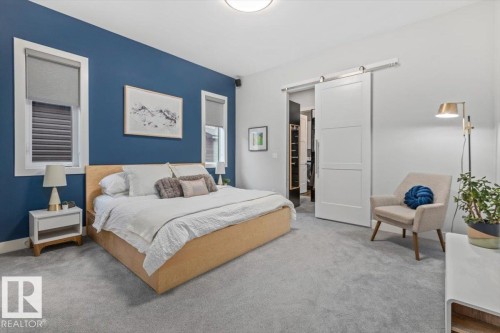 Bedroom featuring a prominent accent wall, two windows with roller shades, and a large sliding barn door - 10611 146 Street Nw, Edmonton, AB - Indoor Photo Showing Bedroom