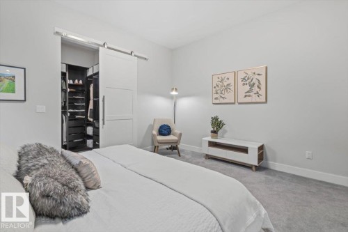 Bedroom featuring a modern barn door entry to a walk-in closet with custom built-in shelving, soft gray carpeting, and white baseboards - 10611 146 Street Nw, Edmonton, AB - Indoor Photo Showing Bedroom