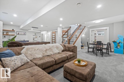 Spacious lower-level entertainment area featuring recessed lighting, light gray carpeting, and a modern staircase with glass paneling and wood-finish railings - 10611 146 Street Nw, Edmonton, AB - Indoor Photo Showing Living Room