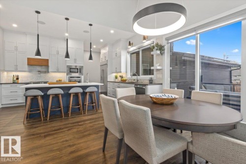 Open-concept kitchen and dining area featuring wood-finish flooring, a kitchen island with seating, white shaker cabinetry, a built-in microwave, and large glass doors - 10611 146 Street Nw, Edmonton, AB - Indoor Photo Showing Dining Room