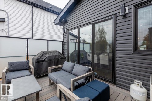 Outdoor deck featuring composite flooring, dark horizontal siding, sliding glass doors, a privacy screen, and an exterior wall sconce - 10611 146 Street Nw, Edmonton, AB - Outdoor With Deck Patio Veranda With Exterior
