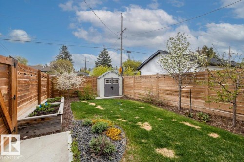 Fenced backyard featuring a manicured lawn, a raised garden bed, a gravel path, mature trees, and a storage shed - 10611 146 Street Nw, Edmonton, AB - Outdoor