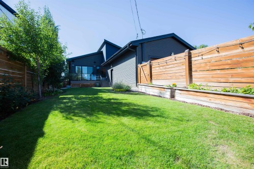 Expansive grassy yard featuring a modern multi-level structure with large windows, an elevated deck with glass railing, and a slatted wood fence with integrated planter boxes - 10611 146 Street Nw, Edmonton, AB - Outdoor With Exterior