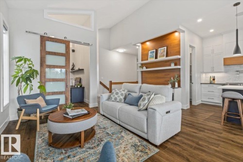 Open-concept living space featuring wood-finish flooring, a contemporary barn door with frosted glass panels, and a built-in shelving unit with recessed lighting - 10611 146 Street Nw, Edmonton, AB - Indoor Photo Showing Living Room