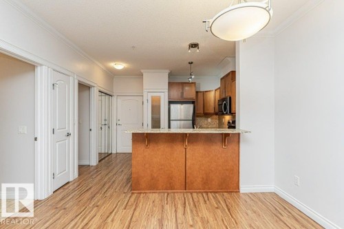 Open-concept living area featuring wood-finish flooring, crown molding, and a kitchen island with a granite countertop - 145 10121 80 Avenue, Edmonton, AB - Indoor Photo Showing Kitchen