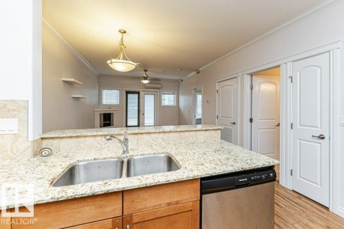 Kitchen area featuring granite countertops, double stainless steel sink, wood-finish flooring, and light wood cabinetry - 145 10121 80 Avenue, Edmonton, AB - Indoor Photo Showing Kitchen With Double Sink
