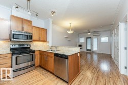 Kitchen featuring wood-finish flooring, stainless steel appliances, light wood cabinetry, and a granite-style countertop with an integrated double basin sink - 