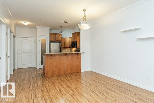 Open-concept living area featuring wood-finish flooring, crown molding, and a kitchen island with seating - 145 10121 80 Avenue, Edmonton, AB - Indoor Photo Showing Kitchen