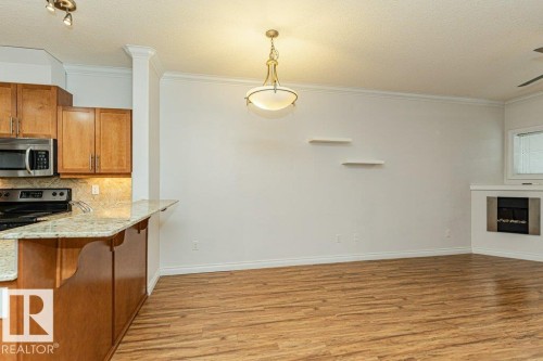 Open-concept living area featuring wood-finish flooring, a built-in electric fireplace, recessed lighting, and a kitchen island with stone countertops - 145 10121 80 Avenue, Edmonton, AB - Indoor Photo Showing Kitchen With Fireplace