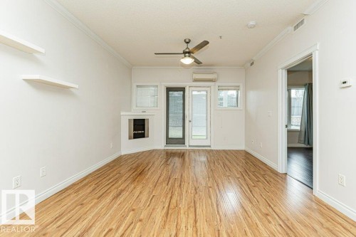 Spacious room featuring wood-finish flooring, a built-in fireplace, a glass-paned exterior door, and a ceiling fan with integrated lighting - 145 10121 80 Avenue, Edmonton, AB - Indoor Photo Showing Other Room