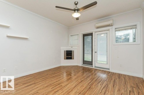 Spacious room featuring wood-finish flooring, a built-in fireplace, a ceiling fan, and multiple windows - 145 10121 80 Avenue, Edmonton, AB - Indoor Photo Showing Other Room With Fireplace