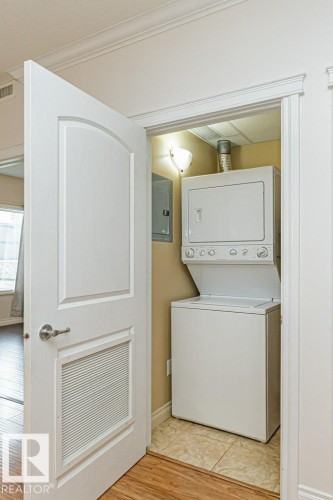Dedicated laundry closet featuring a stacked washer and dryer unit, tiled flooring, built-in wall lighting, and a louvered door - 145 10121 80 Avenue, Edmonton, AB - Indoor Photo Showing Laundry Room