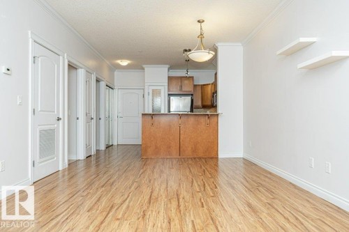 Open-concept living space featuring wood-finish flooring, white walls, and crown molding - 145 10121 80 Avenue, Edmonton, AB - Indoor