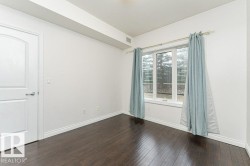 Spacious room featuring dark wood-finish flooring, a large multi-pane window, bright white walls, and elegant white baseboards - 