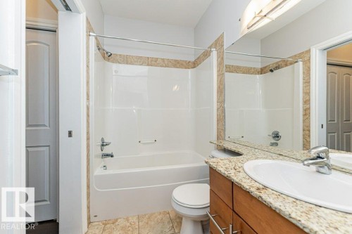 Bathroom featuring a tub and shower combination with tiled surround, a vanity with a light-toned countertop, and wood-finish cabinetry - 145 10121 80 Avenue, Edmonton, AB - Indoor Photo Showing Bathroom