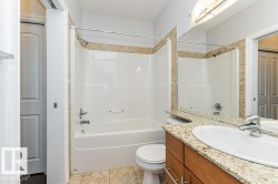 Bathroom featuring a tub and shower combination with tiled surround, a vanity with a light-toned countertop, and wood-finish cabinetry - 