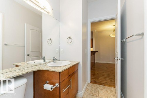 Bathroom vanity featuring dual under-mount sinks, a stone-finish countertop, and wood-finish cabinetry with brushed nickel hardware - 145 10121 80 Avenue, Edmonton, AB - Indoor Photo Showing Bathroom