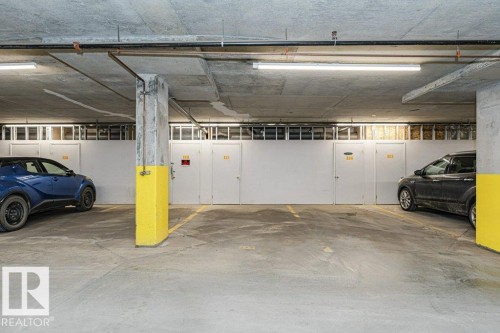 Underground parking garage featuring concrete flooring and ceiling, fluorescent lighting, and individual storage units with white doors - 145 10121 80 Avenue, Edmonton, AB - Indoor Photo Showing Garage