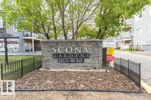 Stone-clad entrance monument featuring a black metal fence and landscaped wood chip beds - 145 10121 80 Avenue, Edmonton, AB - Outdoor