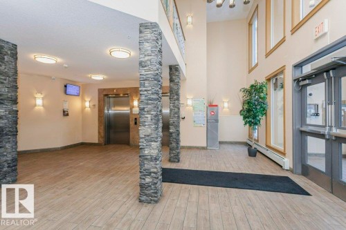 Spacious building foyer featuring stone-clad columns, wood-finish flooring, recessed lighting, and a stainless steel elevator - 145 10121 80 Avenue, Edmonton, AB - Indoor Photo Showing Other Room