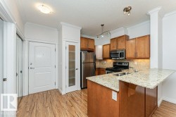 Kitchen featuring stainless steel appliances, wood-finish cabinetry, a dual basin sink, light granite countertops, and wood-finish flooring - 
