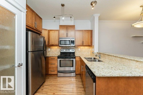 Kitchen featuring wood-finish flooring, stainless steel appliances, light wood cabinetry, and a double basin sink - 145 10121 80 Avenue, Edmonton, AB - Indoor Photo Showing Kitchen With Stainless Steel Kitchen With Double Sink