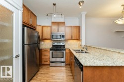 Kitchen featuring wood-finish flooring, stainless steel appliances, light wood cabinetry, and a double basin sink - 