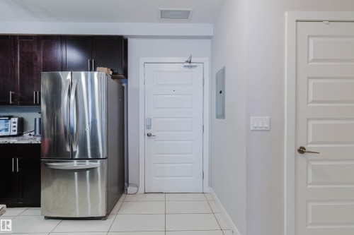 Kitchen area featuring a stainless steel refrigerator, dark wood-finish cabinetry, and light-toned countertop - 510 5151 Windermere Boulevard, Edmonton, AB - Indoor Photo Showing Kitchen