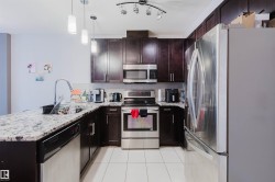 Kitchen featuring dark wood cabinetry, light-toned granite-style countertops, and stainless steel appliances including a range, microwave, and refrigerator - 