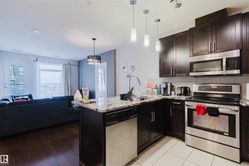 Modern kitchen featuring dark wood cabinetry, stainless steel appliances, granite countertops, and a subway tile backsplash - 510 5151 Windermere Boulevard, Edmonton, AB - Indoor Photo Showing Kitchen With Upgraded Kitchen