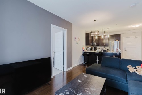 Contemporary kitchen featuring dark wood cabinetry, stainless steel appliances, and a breakfast bar with pendant lighting - 510 5151 Windermere Boulevard, Edmonton, AB - Indoor Photo Showing Living Room