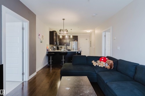 Open-concept living area featuring wood-finish flooring, a kitchen island with seating, dark wood cabinetry, stainless steel appliances, and recessed lighting - 510 5151 Windermere Boulevard, Edmonton, AB - Indoor Photo Showing Living Room
