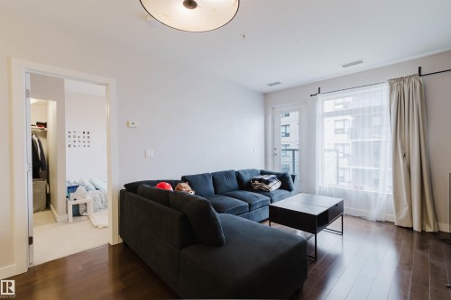 Spacious living area featuring wood-finish flooring, a contemporary ceiling light fixture, and large windows with a glass-paneled door - 510 5151 Windermere Boulevard, Edmonton, AB - Indoor Photo Showing Living Room