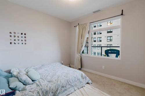 Bedroom featuring neutral painted walls, carpeted flooring, a large window, and a roller blind - 510 5151 Windermere Boulevard, Edmonton, AB - Indoor Photo Showing Bedroom