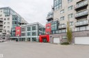 Contemporary multi-story building featuring a prominent red entrance, extensive glass facades, private balconies with glass railings, a stone-clad base, and integrated garage doors - 510 5151 Windermere Boulevard, Edmonton, AB  - Outdoor With Balcony 