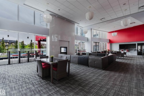 Spacious common area featuring full-height windows, a prominent fireplace, and an expansive wall-mounted entertainment area - 510 5151 Windermere Boulevard, Edmonton, AB - Indoor Photo Showing Other Room
