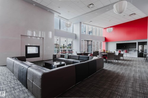 Spacious lounge area featuring a large built-in fireplace, high ceilings, expansive windows, and durable patterned carpeting - 510 5151 Windermere Boulevard, Edmonton, AB - Indoor