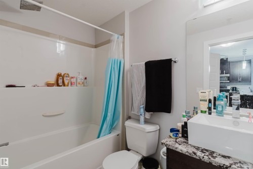 Bathroom featuring a white tub/shower combination with a built-in shelf, a contemporary rectangular vessel sink, a granite-finish countertop, a large wall-mounted mirror, and a chrome towel bar - 510 5151 Windermere Boulevard, Edmonton, AB - Indoor Photo Showing Bathroom