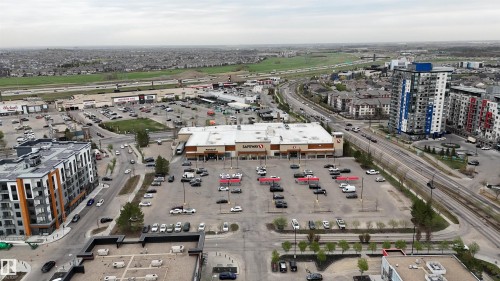 Aerial perspective showcasing an urban landscape with multiple multi-story residential buildings, a commercial center featuring a large grocery store, and extensive parking areas - 510 5151 Windermere Boulevard, Edmonton, AB - Outdoor With View