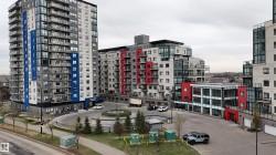 Contemporary multi-story building featuring a blue and grey facade, individual balconies with glass railings, a circular drive with central landscaping, and a street-level entrance - 