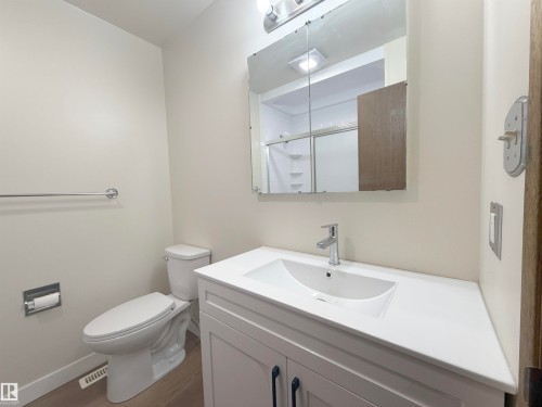 Modern bathroom featuring a single vanity with a white countertop and integrated sink, chrome faucet, and storage cabinetry with dark hardware - 1731 51 Street, Edmonton, AB - Indoor Photo Showing Bathroom