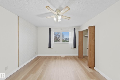 Spacious room featuring light wood-finish flooring, a ceiling fan with integrated lighting, a window with dark drapery, and a bi-fold door closet - 1731 51 Street, Edmonton, AB - Indoor Photo Showing Other Room