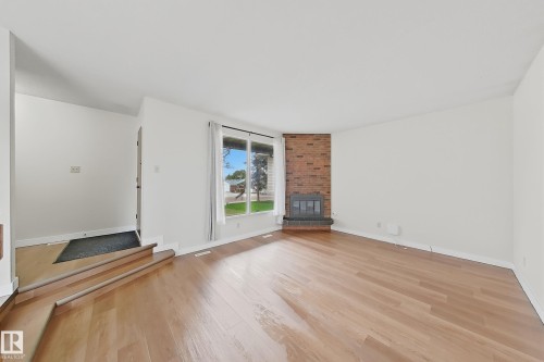Spacious living area featuring wood-finish flooring, a prominent brick fireplace with hearth, and large windows providing ample natural light - 1731 51 Street, Edmonton, AB - Indoor