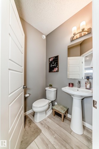 Pedestal sink with chrome faucet, light wood-finish flooring, white toilet, wall-mounted vanity lighting, and paneled interior door - 38 Prospect Place, Spruce Grove, AB - Indoor Photo Showing Bathroom