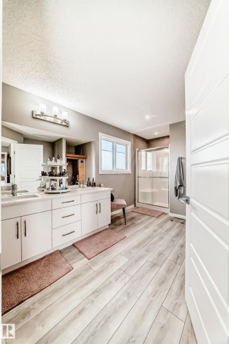 Spacious bathroom featuring an expansive double vanity with white cabinetry, light-toned wood-finish flooring, a contemporary shower enclosure, recessed lighting, and a horizontal window providing natural light - 38 Prospect Place, Spruce Grove, AB - Indoor