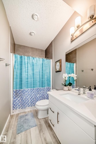 Modern bathroom featuring a white vanity with a rectangular sink, a contemporary three-light fixture, and wood-finish flooring - 38 Prospect Place, Spruce Grove, AB - Indoor Photo Showing Bathroom