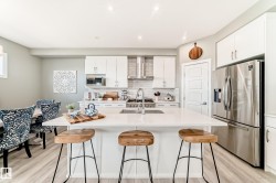 Modern kitchen featuring a large central island with a solid surface countertop, white shaker-style cabinetry, stainless steel appliances, and wood-finish flooring - 