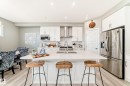 Modern kitchen featuring a large central island with a solid surface countertop, white shaker-style cabinetry, stainless steel appliances, and wood-finish flooring - 38 Prospect Place, Spruce Grove, AB  - Indoor Photo Showing Kitchen 