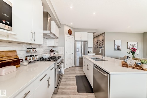 Spacious kitchen featuring white cabinetry, light countertops, subway tile backsplash, stainless steel appliances, and a large center island with an undermount double-basin sink - 38 Prospect Place, Spruce Grove, AB - Indoor Photo Showing Kitchen With Double Sink With Upgraded Kitchen